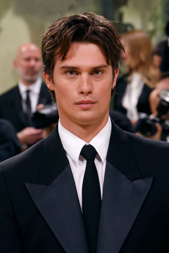 Nicholas Galitzine in a black suit and tie with photographers in the background