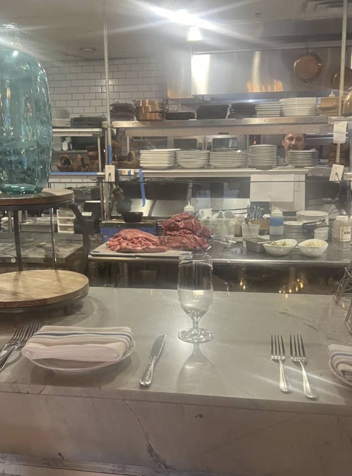 Restaurant interior with raw steaks on display, a set table in the foreground, and chef visible in the background