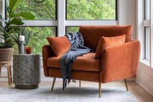 A velvet orange sofa with a gray throw blanket
