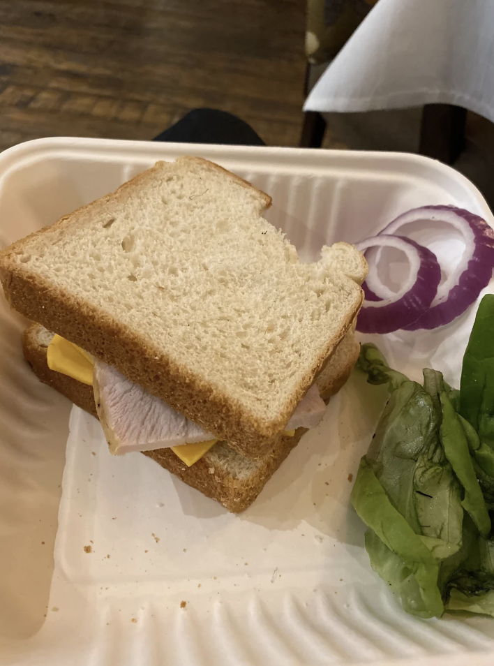 Turkey and cheese sandwich on a plate with a side of lettuce and sliced onion