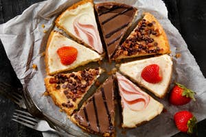 A variety of cheesecake slices with toppings like strawberries and chocolate chips, arranged in a circle on a parchment lined plate
