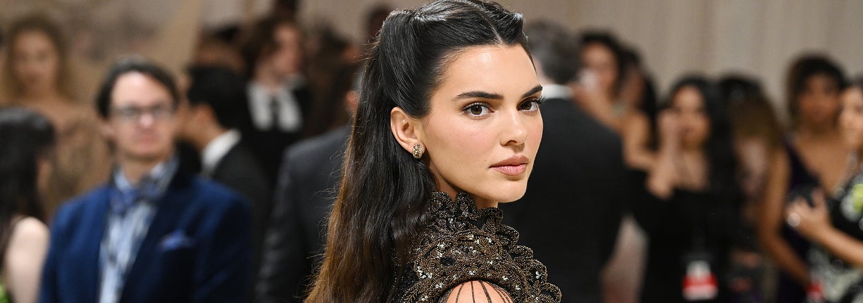 Kendall Jenner in an elegant black lace gown at a formal event. She is looking over her shoulder