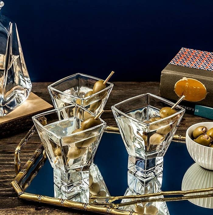 Martini glasses with olives connected  a mirrored tray adjacent  to books