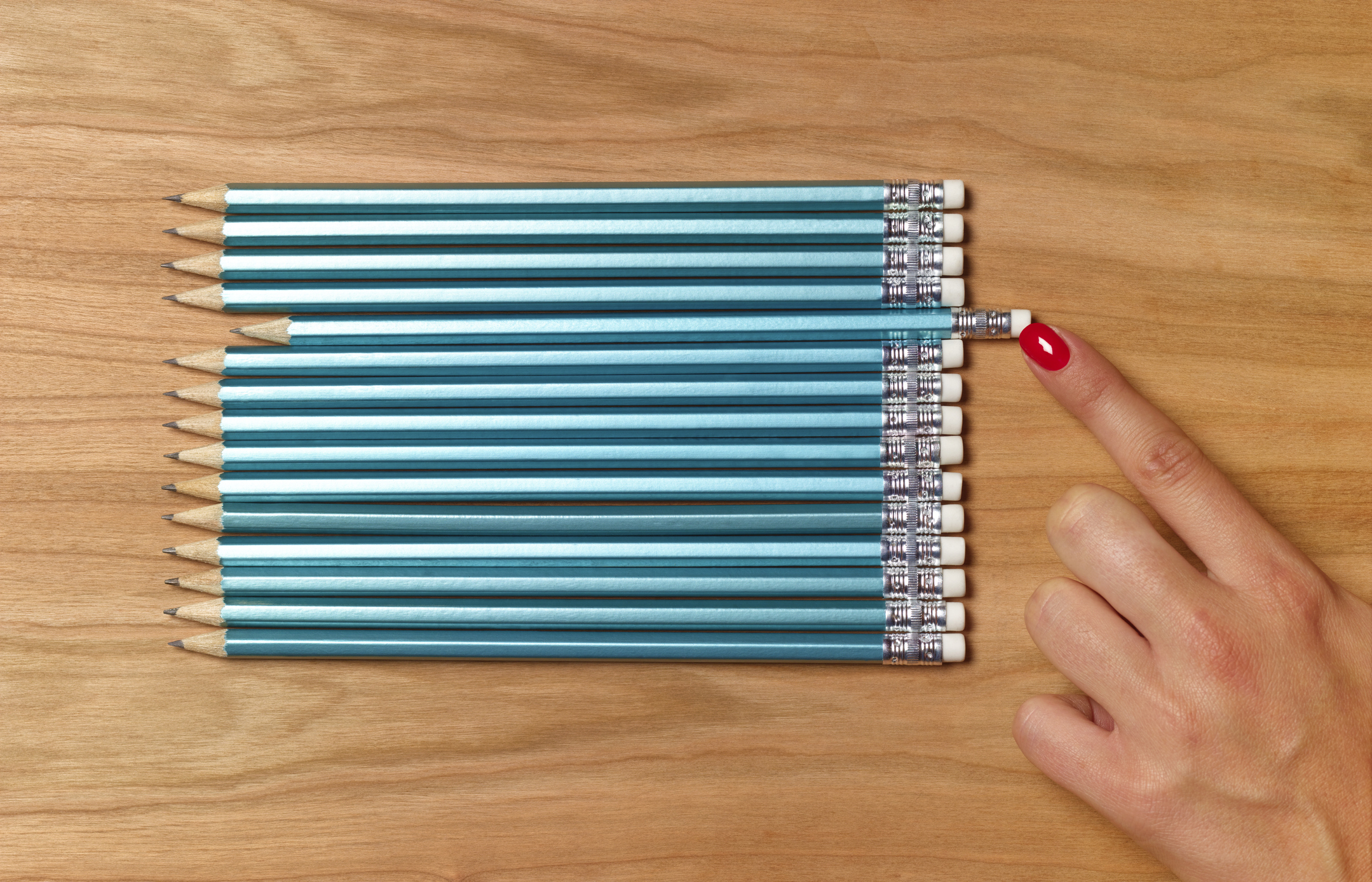 A finger pointing to one pencil among many aligned on a wooden surface, emphasizing selection or decision-making