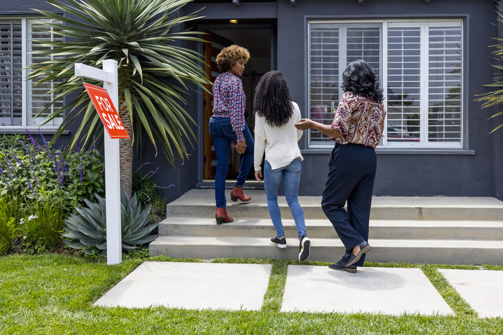 Family walking towards a house with a "For Sale" sign, likely viewing a home