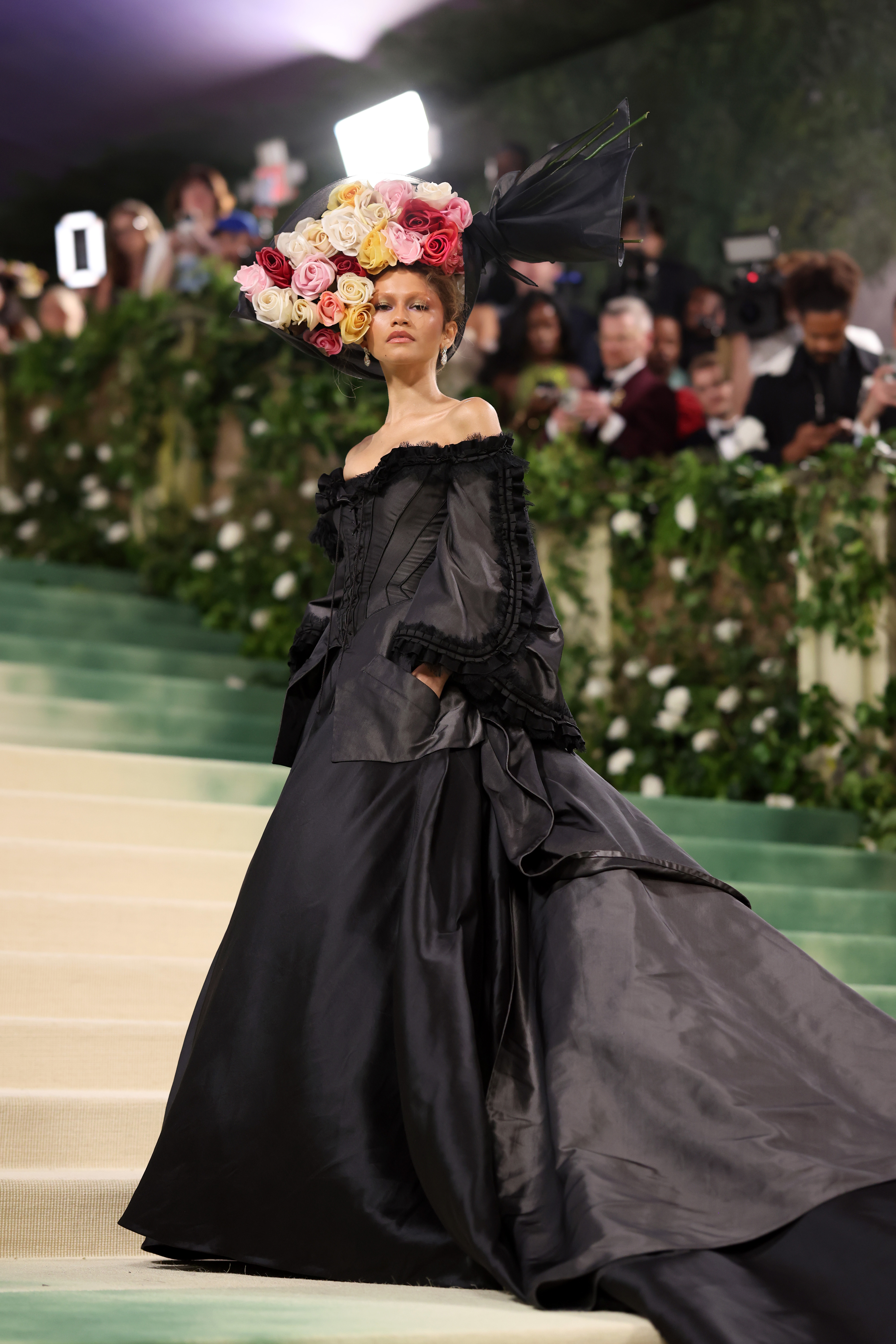 Zendaya in elaborate black gown with large floral headpiece on a staircase at an event