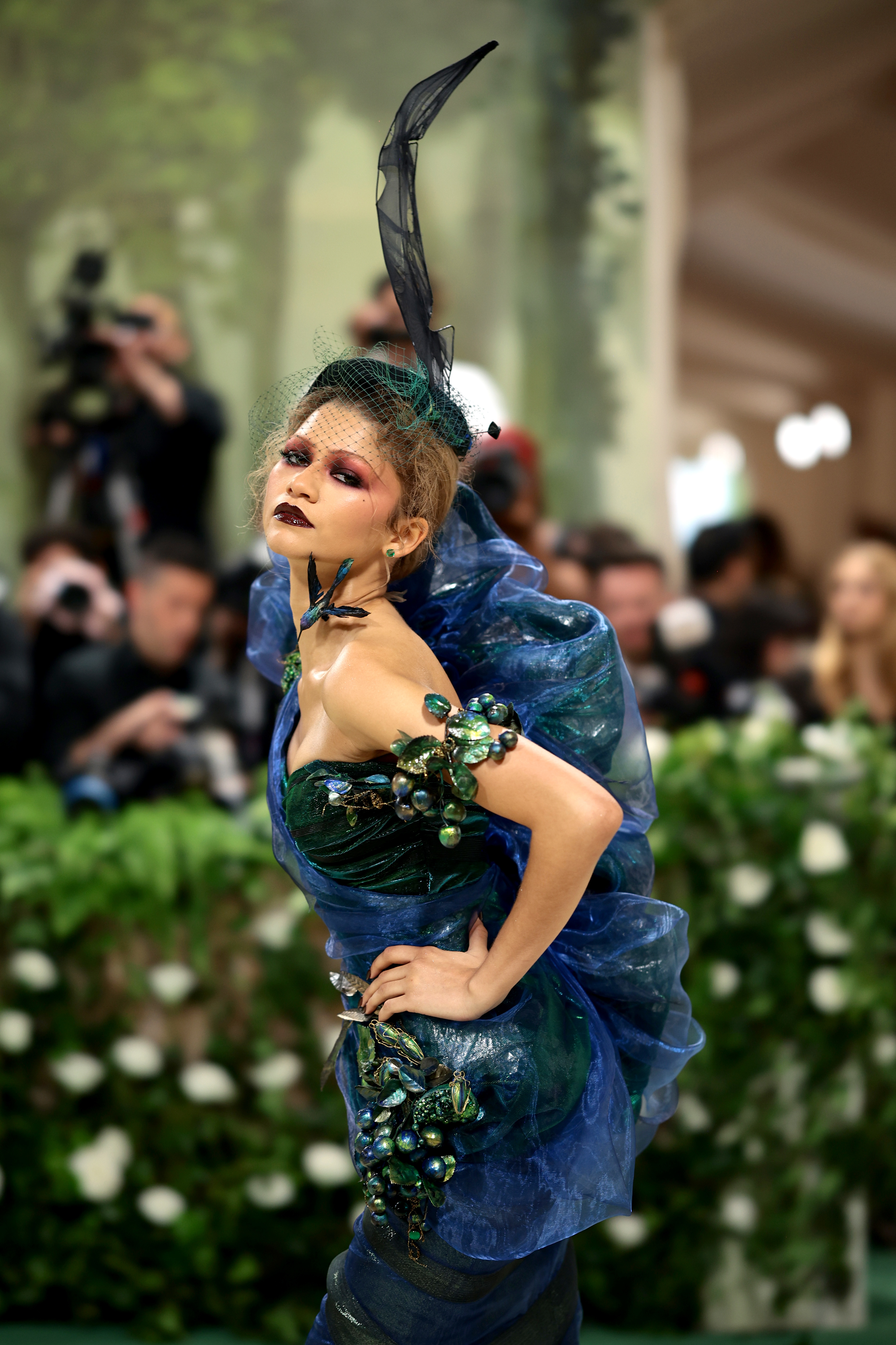 Zendaya in elaborate blue ruffled gown with black feathered headpiece at event