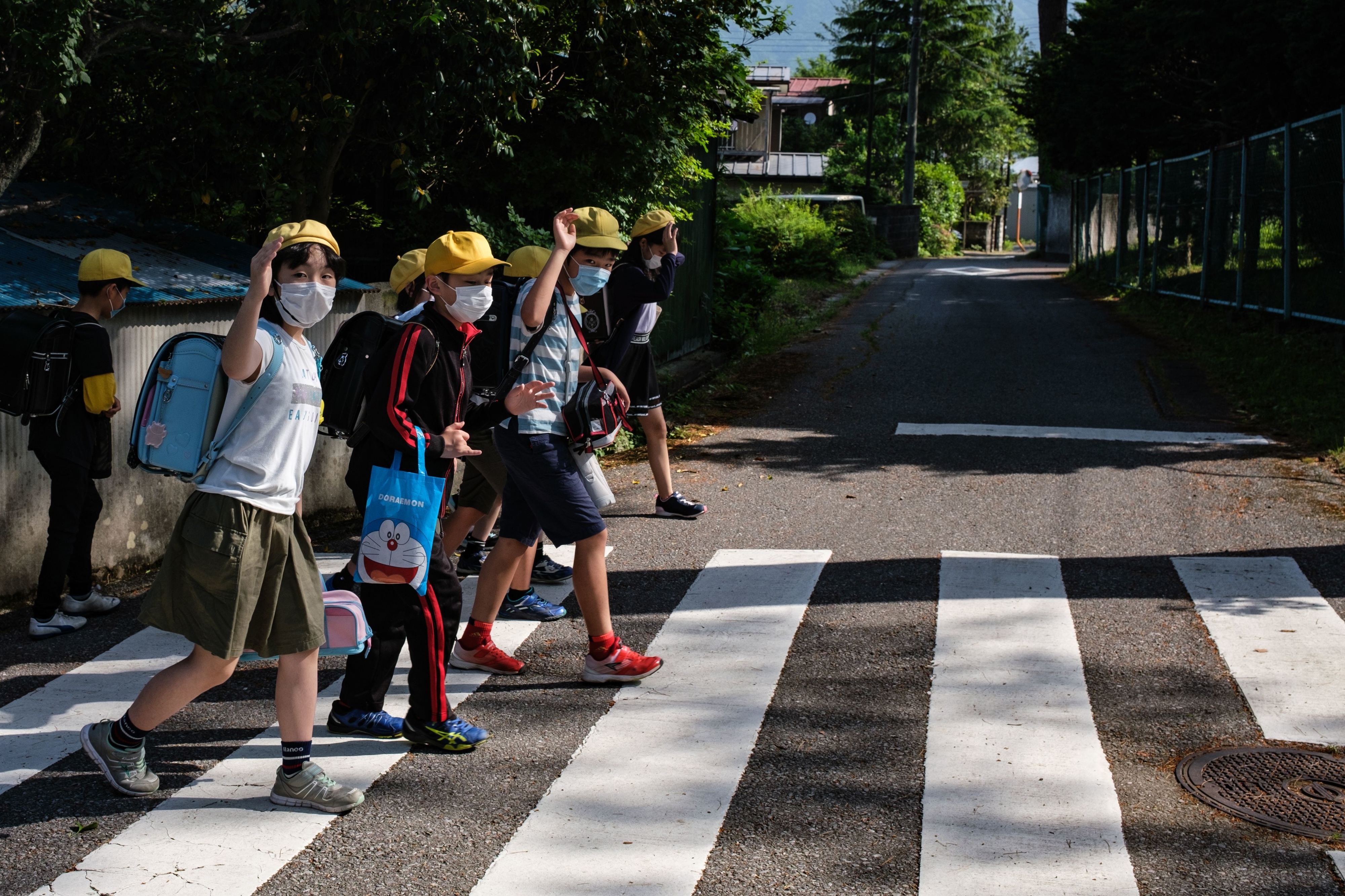 Group of schoolchildren with masks crossing the street safely at a pedestrian crosswalk