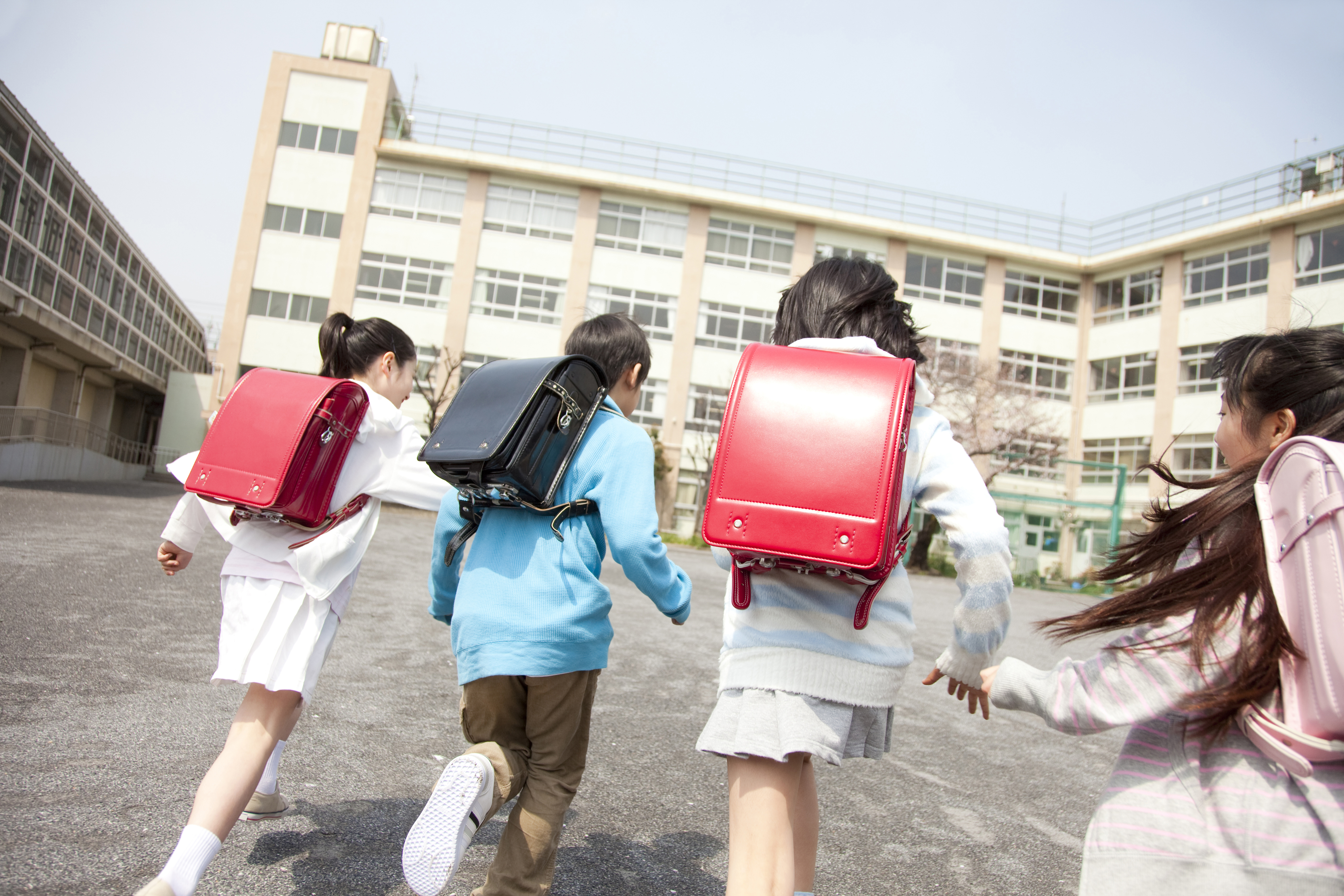 Four students with backpacks running joyfully in a schoolyard