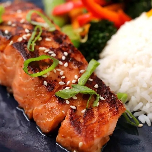 Grilled salmon topped with sesame seeds and green onions, served with rice and vegetables
