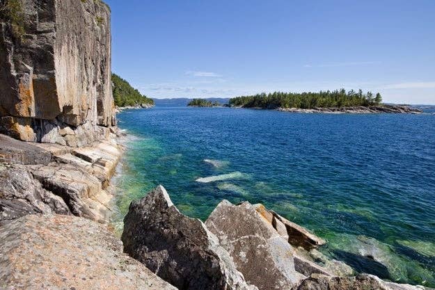 Rocky coastline with a cliff on the left, overlooking a clear water body leading to distant islands