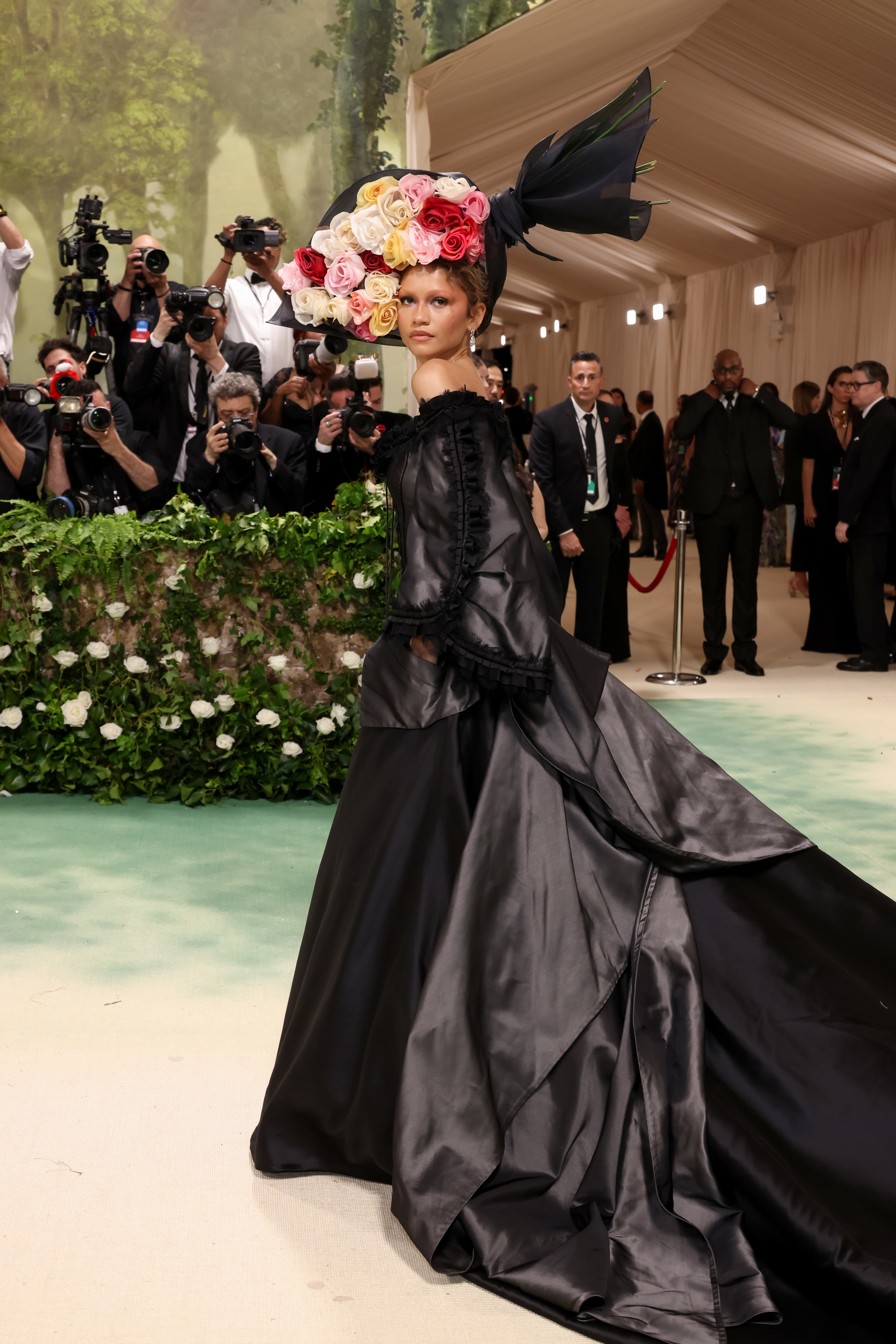 Zendaya in elaborate floral headpiece and black gown at event, photographers in background