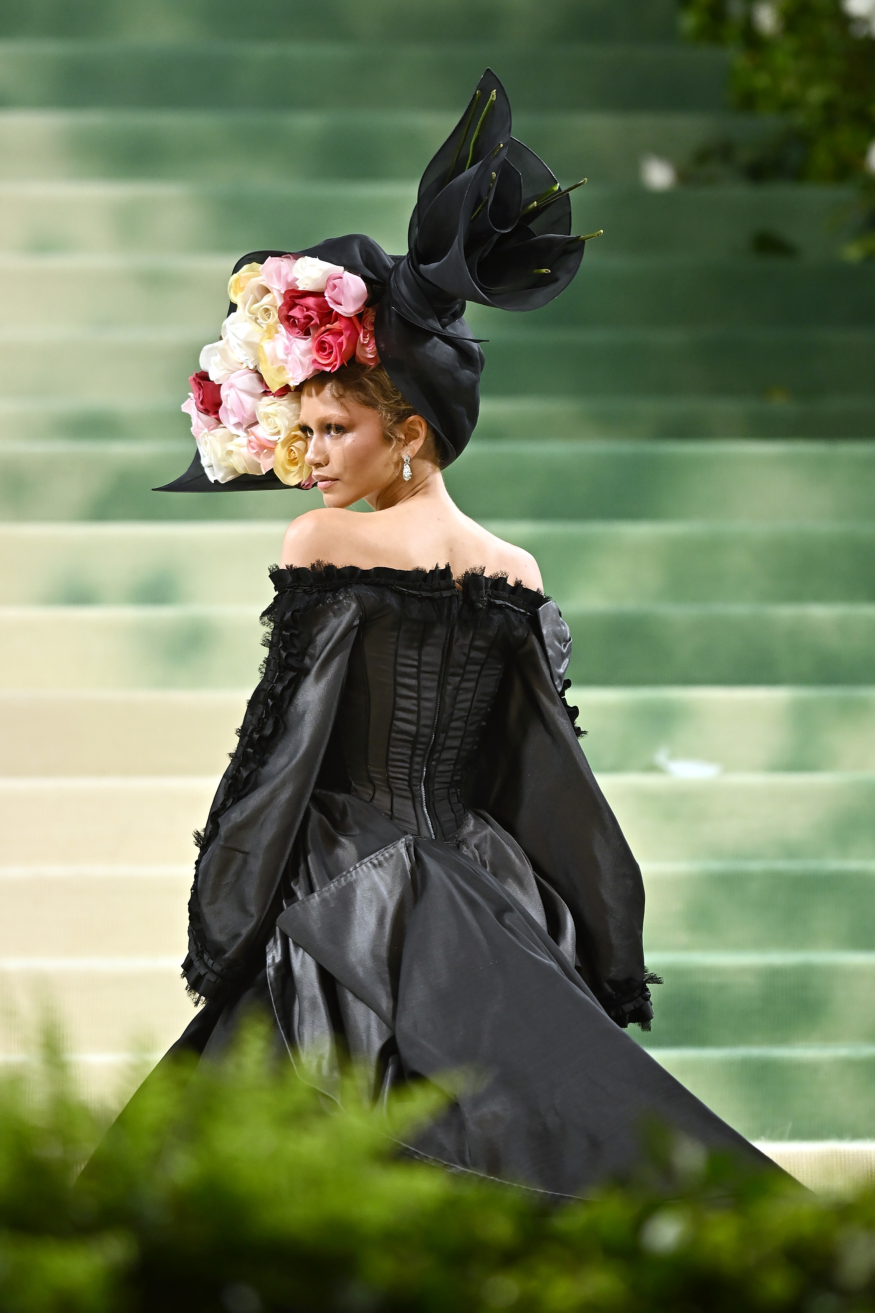 Zendaya in a dramatic black outfit with a large floral hat at an event