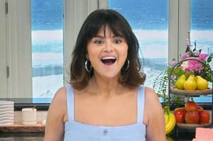 Selena Gomez smiling in a kitchen with a beach view, wearing a casual sleeveless top