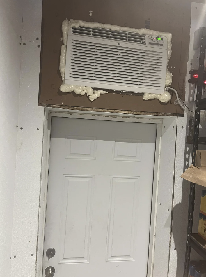 An air conditioning unit mounted above a door, surrounded by foam insulation in an indoor setting