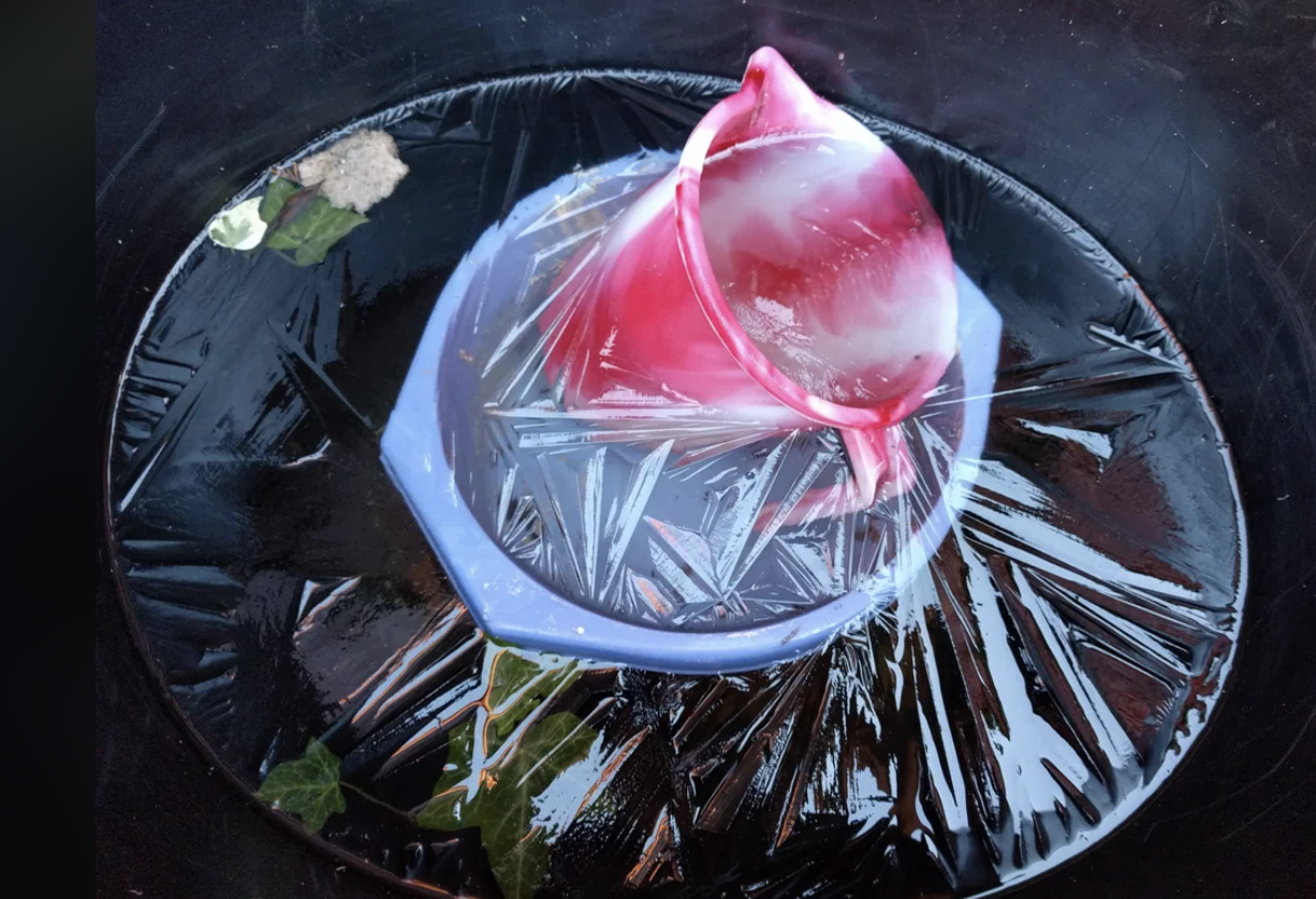 A frozen rose inside a clear ice block, resting on a black patterned surface