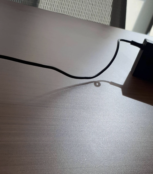 Charging cable plugged into a device on a desk, casting a shadow in sunlight