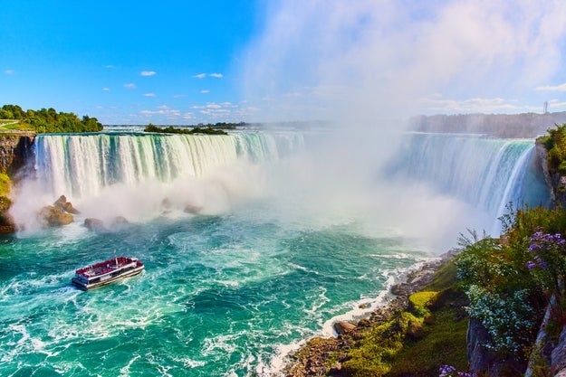 Boat near base of Niagara Falls with mist rising, surrounded by greenery