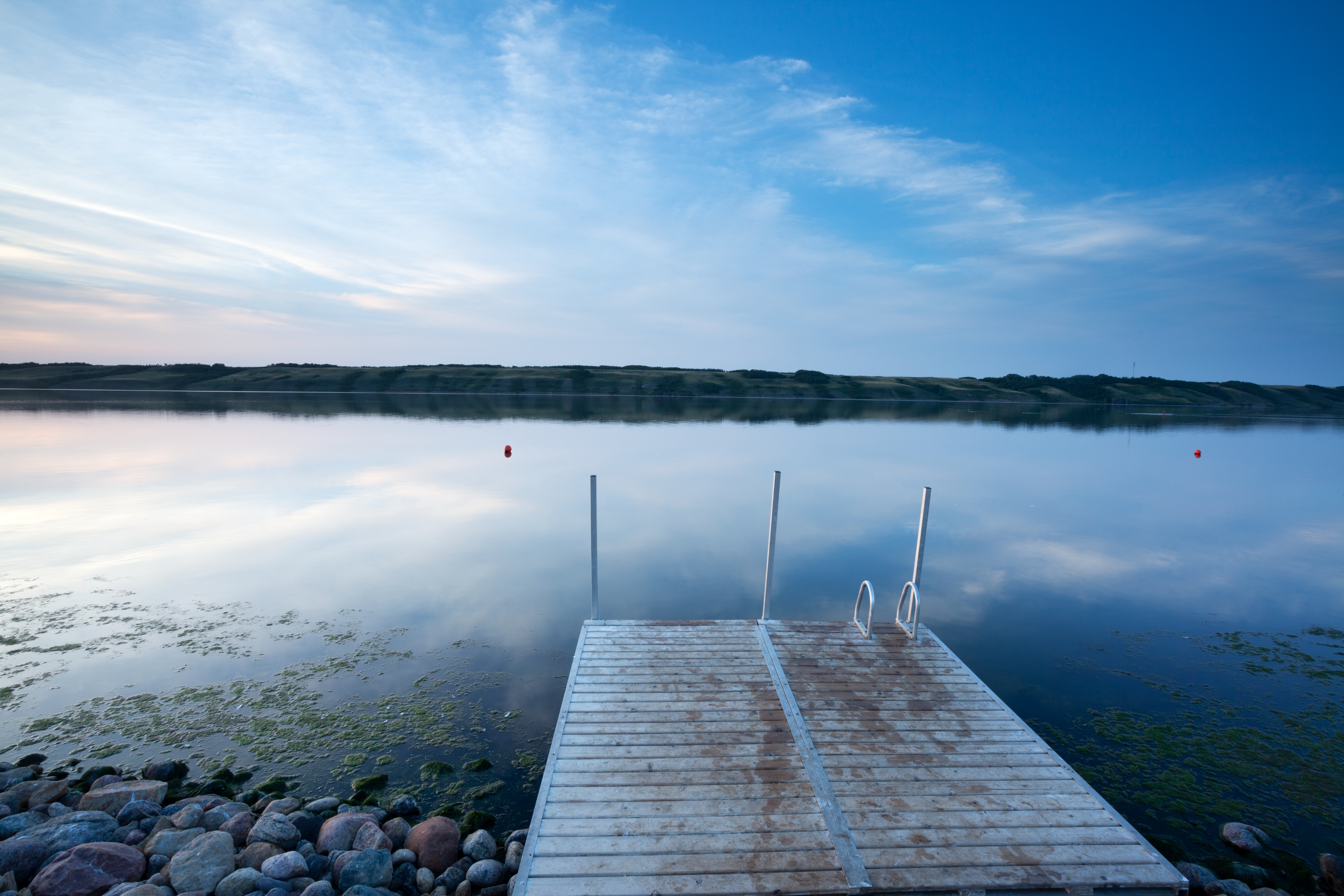 Calm lake with a dock leading into the water at dusk, reflecting the sky, no persons present