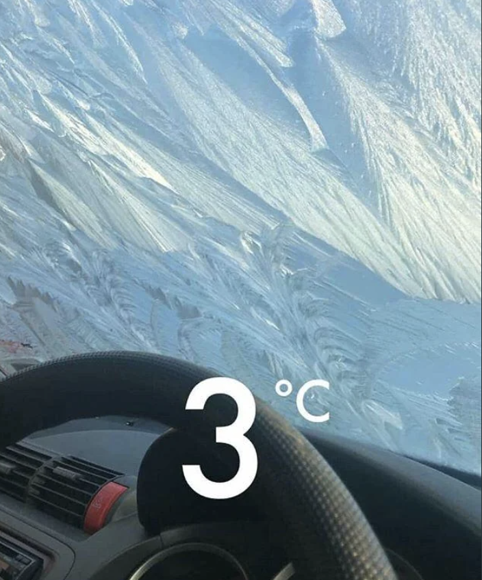 Car dashboard showing 3°C with a snow-covered road ahead, indicating cold driving conditions
