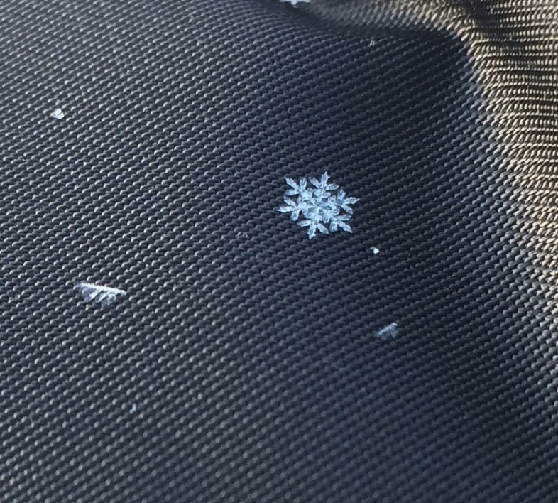 A single snowflake with intricate patterns resting on a woven fabric surface