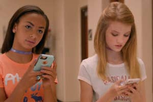 Two girls texting on phones, one wearing a choker and orange shirt, the other in pink