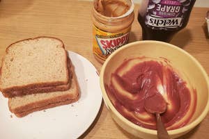 Peanut butter and jelly sandwich in progress with a knife spreading jelly in a bowl, Skippy peanut butter jar, and Welch's jelly