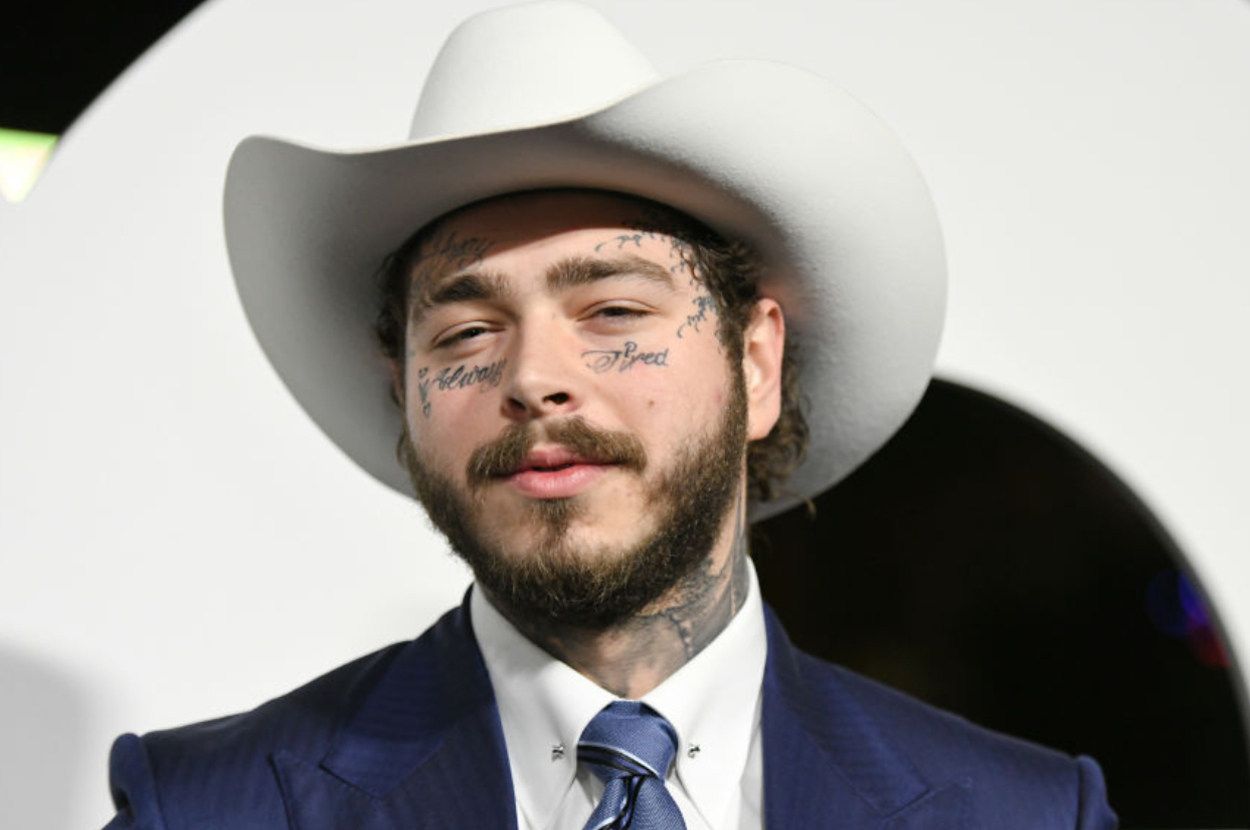 Man in cowboy hat and suit, with facial tattoos visible