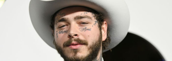 Man in cowboy hat and suit, with facial tattoos visible