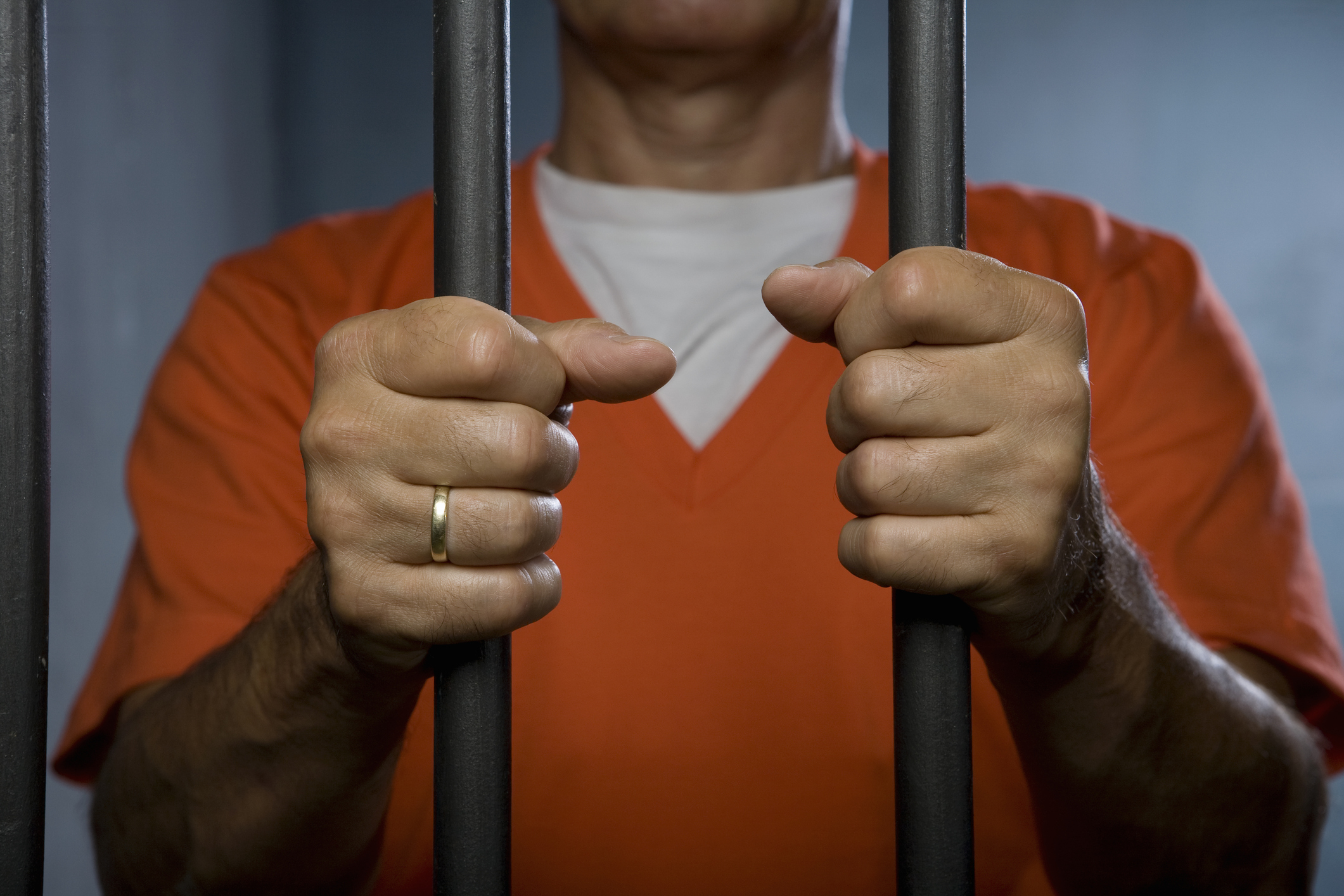 Person in an orange shirt holding onto jail bars