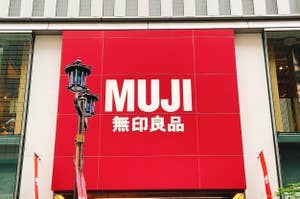 Large MUJI store sign with logo and Japanese text, affixed on a red background above street level