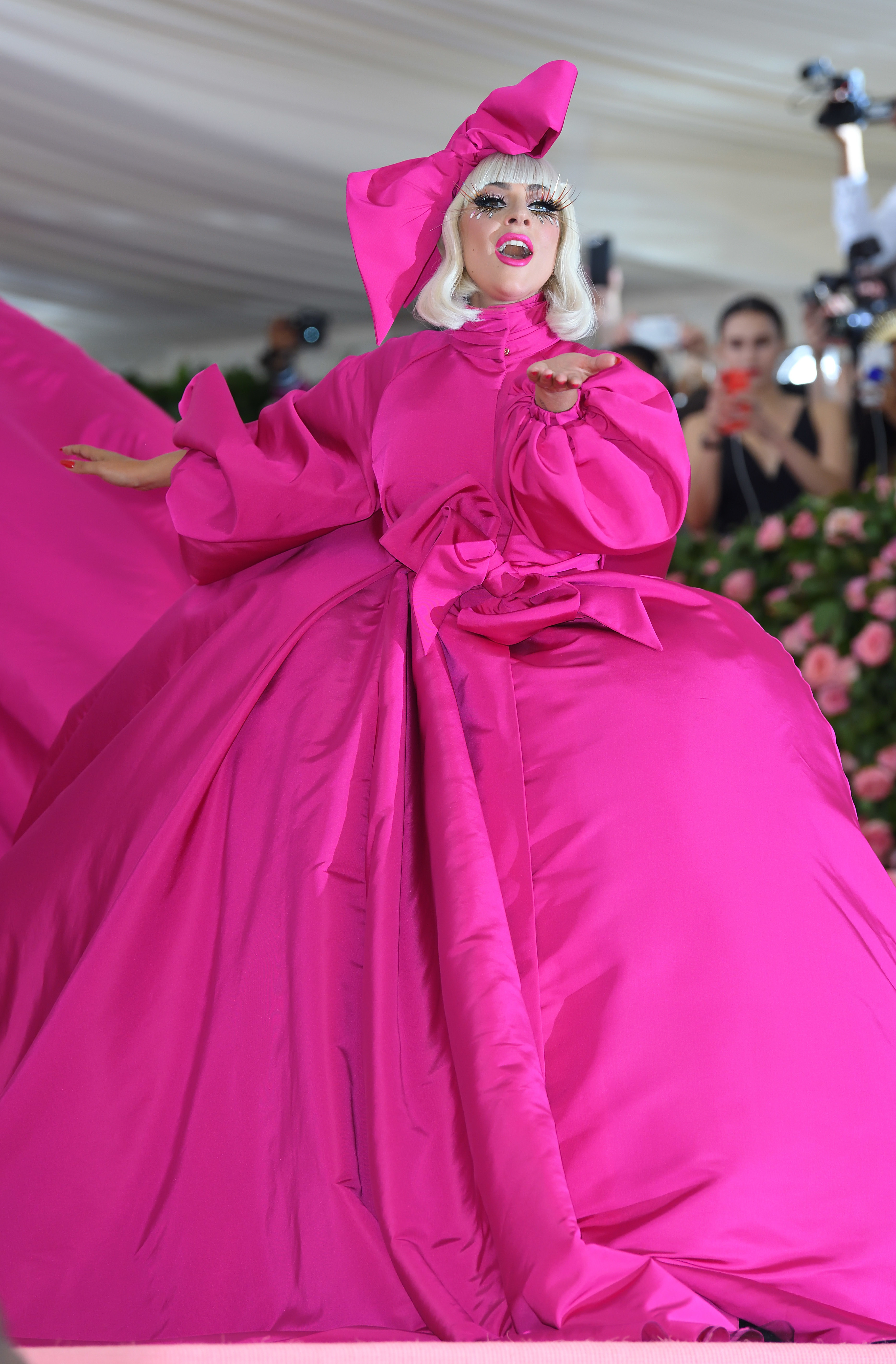 Lady Gaga at the Met Gala in an extravagant pink gown/overcoat with a large bow and matching headpiece