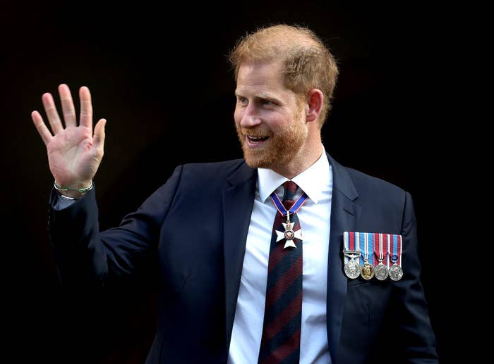 Prince Harry in a suit with medals, waving his hand