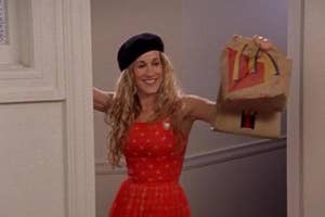 Phoebe Buffay from Friends smiles holding a paper bag, styled in a red polka dot dress and black beret