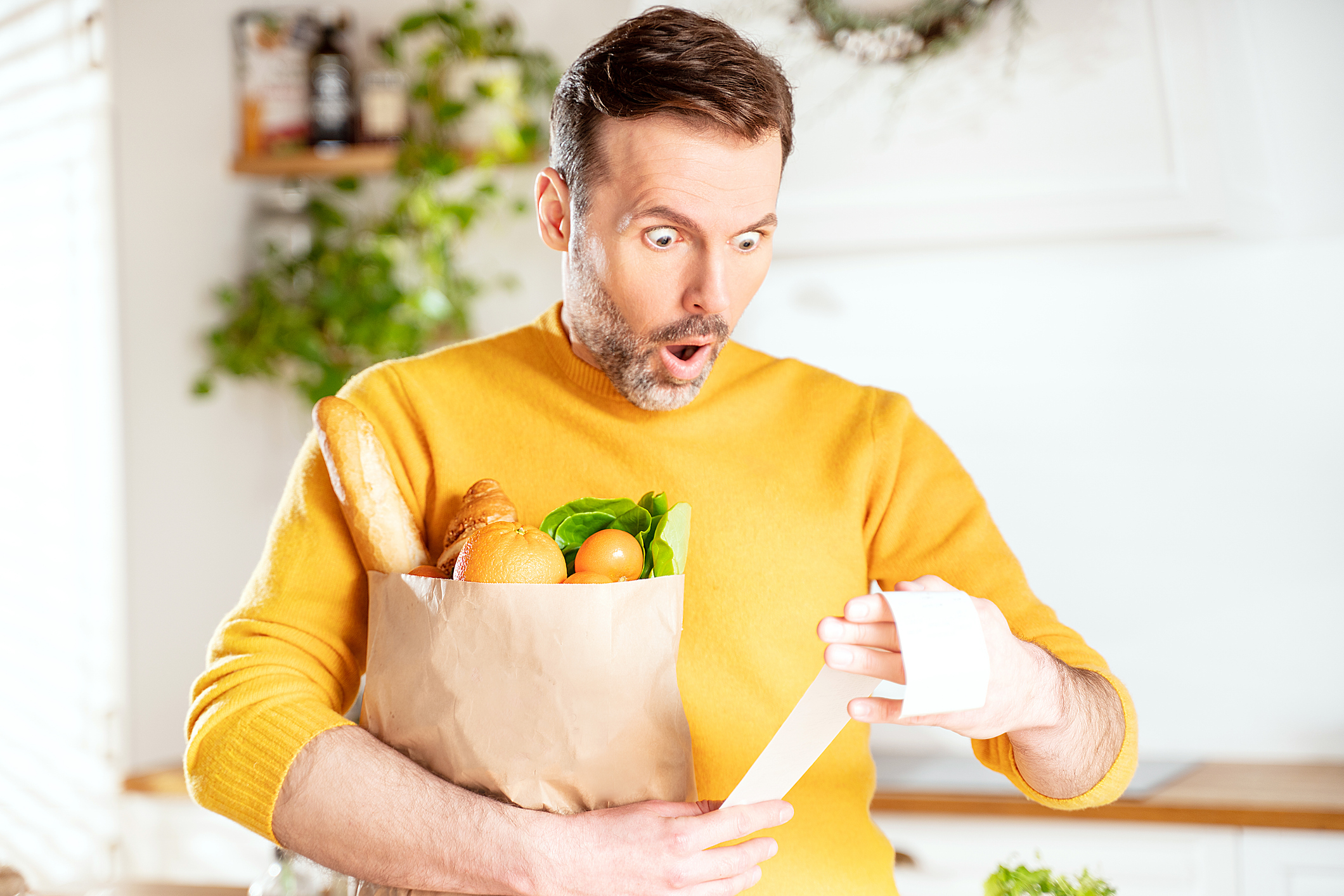 A surprised person holding a grocery bag and looking at a receipt