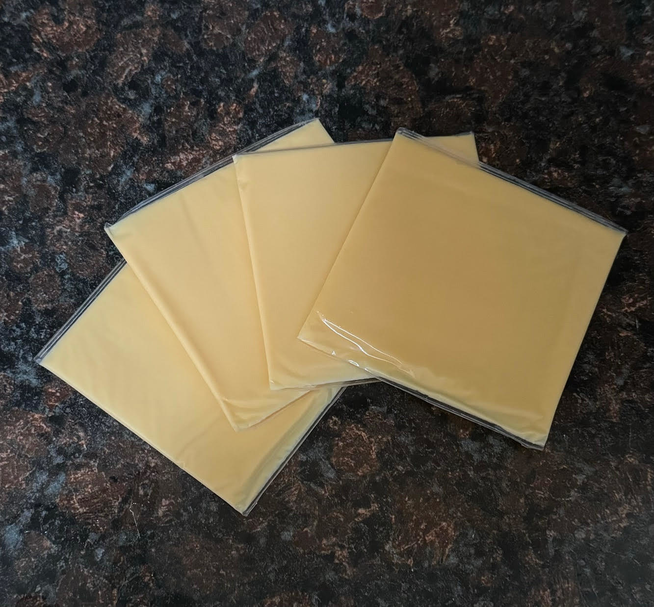 Three slices of processed cheese in plastic wrappers on a countertop