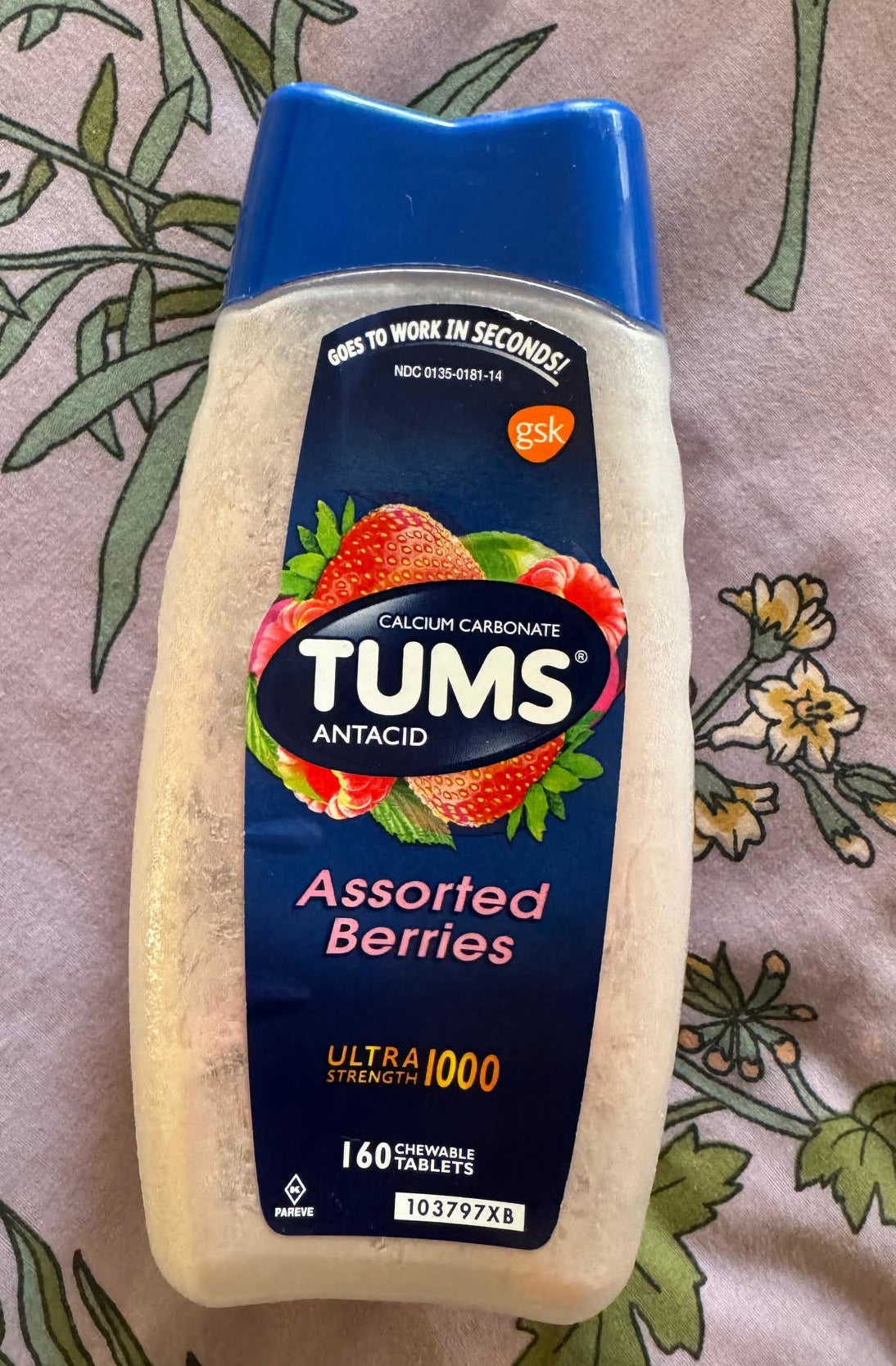 Bottle of TUMS Antacid with &#x27;Assorted Berries&#x27; flavor lying on a floral background