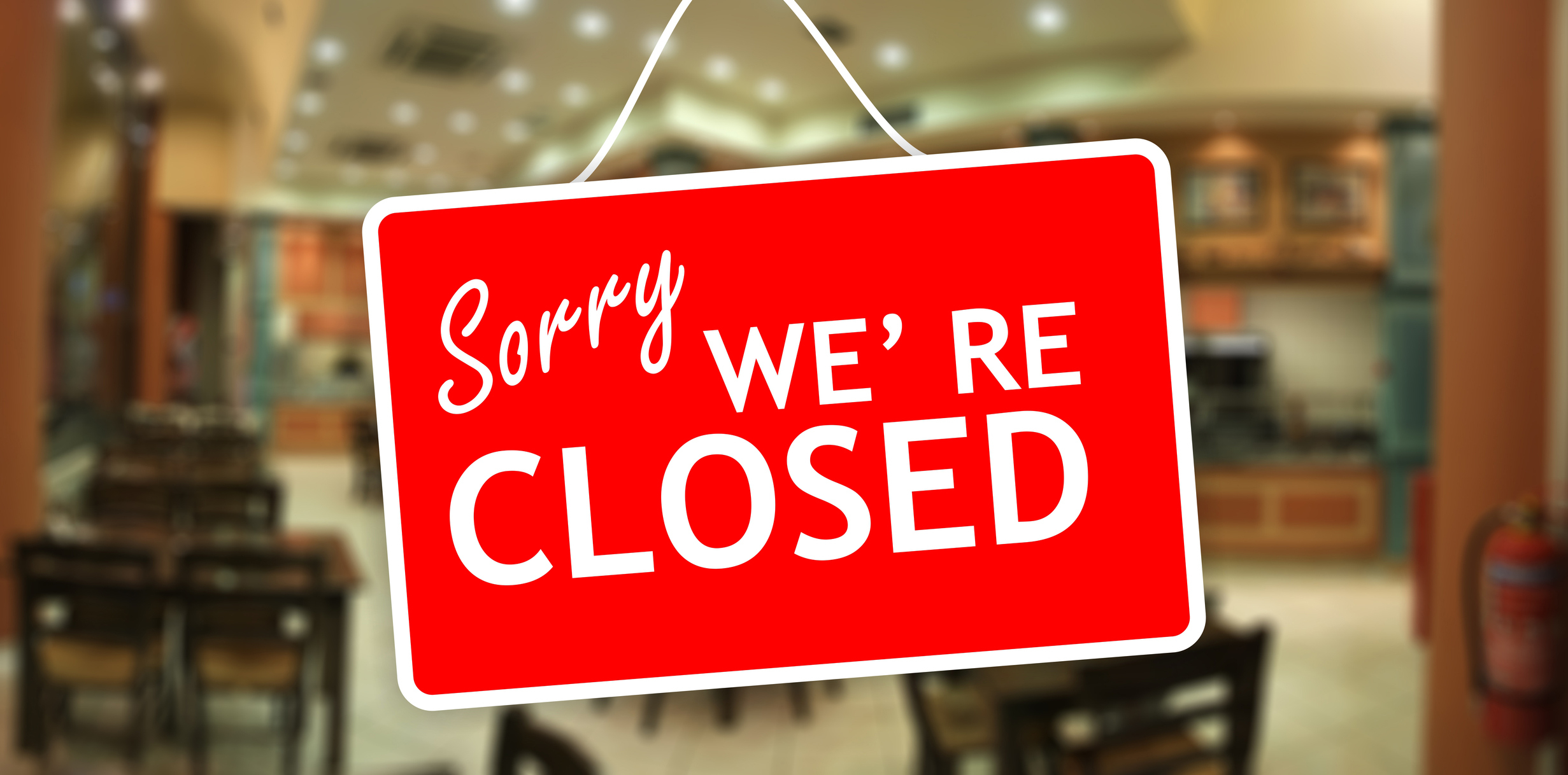 Sign reads &quot;Sorry WE&#x27;RE CLOSED&quot; hanging on a blurry background, possibly inside a shop