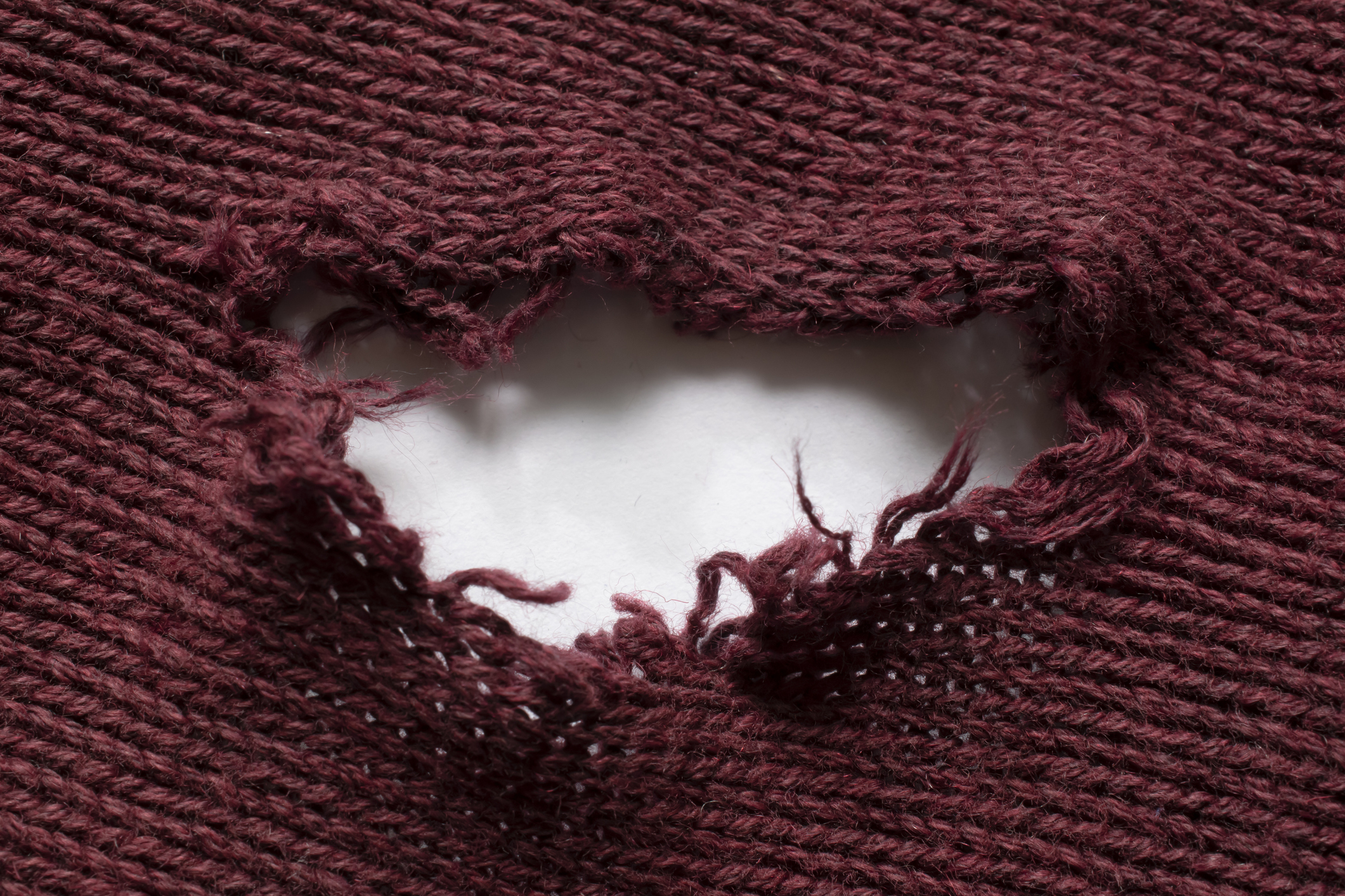 A close-up of a torn knit fabric revealing a white background