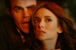 Stefan and Katharine in a dramatic scene, Stefan behind her, each with a surprised expression and fire lighting up their faces