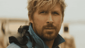 Ryan Gosling with beard and blue jacket facing forward, outdoors, slight squint, serious expression