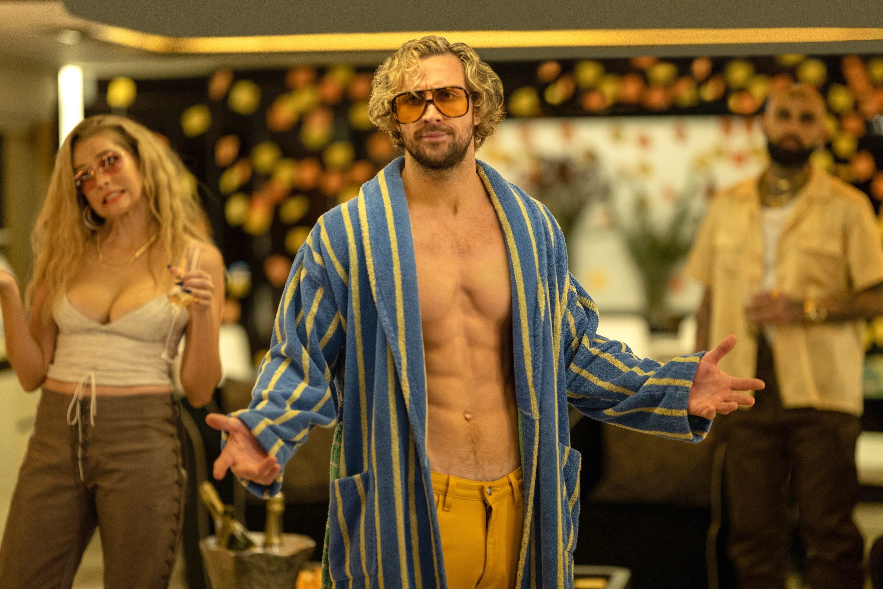 Aaron Taylor-Johnson in a party scene wearing a striped robe with two people standing in the background