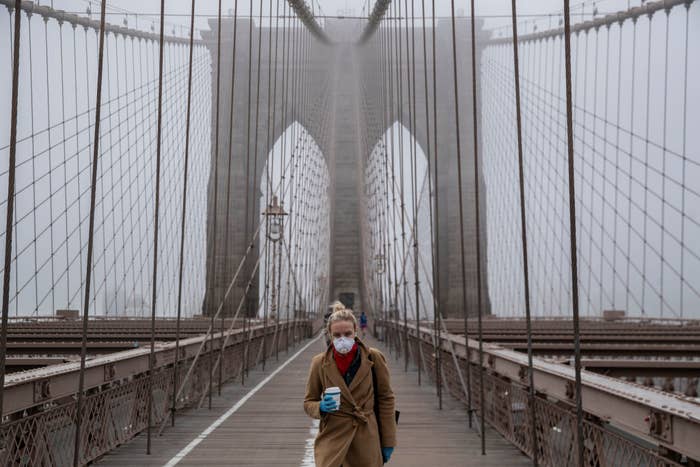 Person with mask holding a drink on Brooklyn Bridge with foggy background