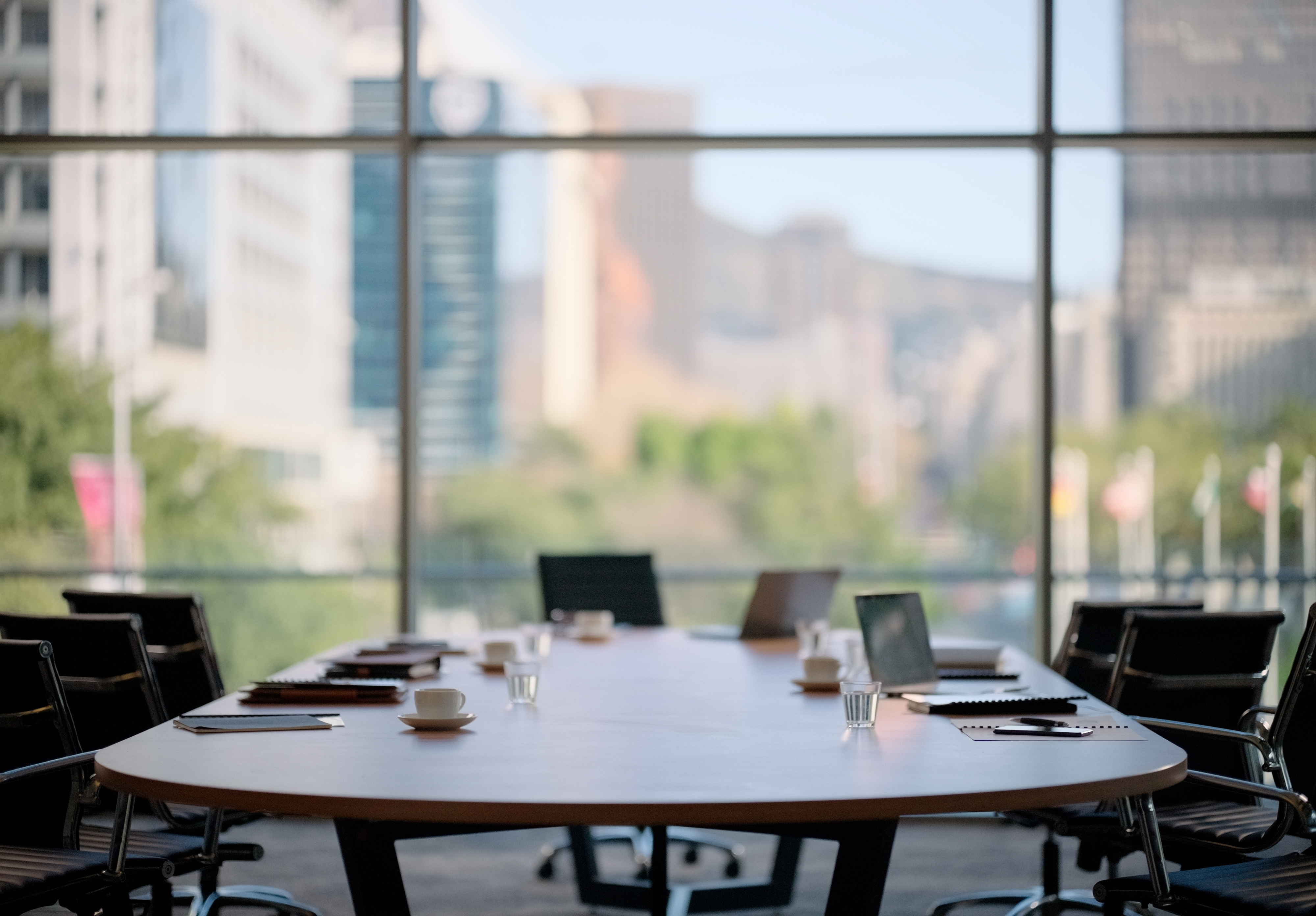 Empty boardroom with large table, chairs, and a cityscape visible through the window