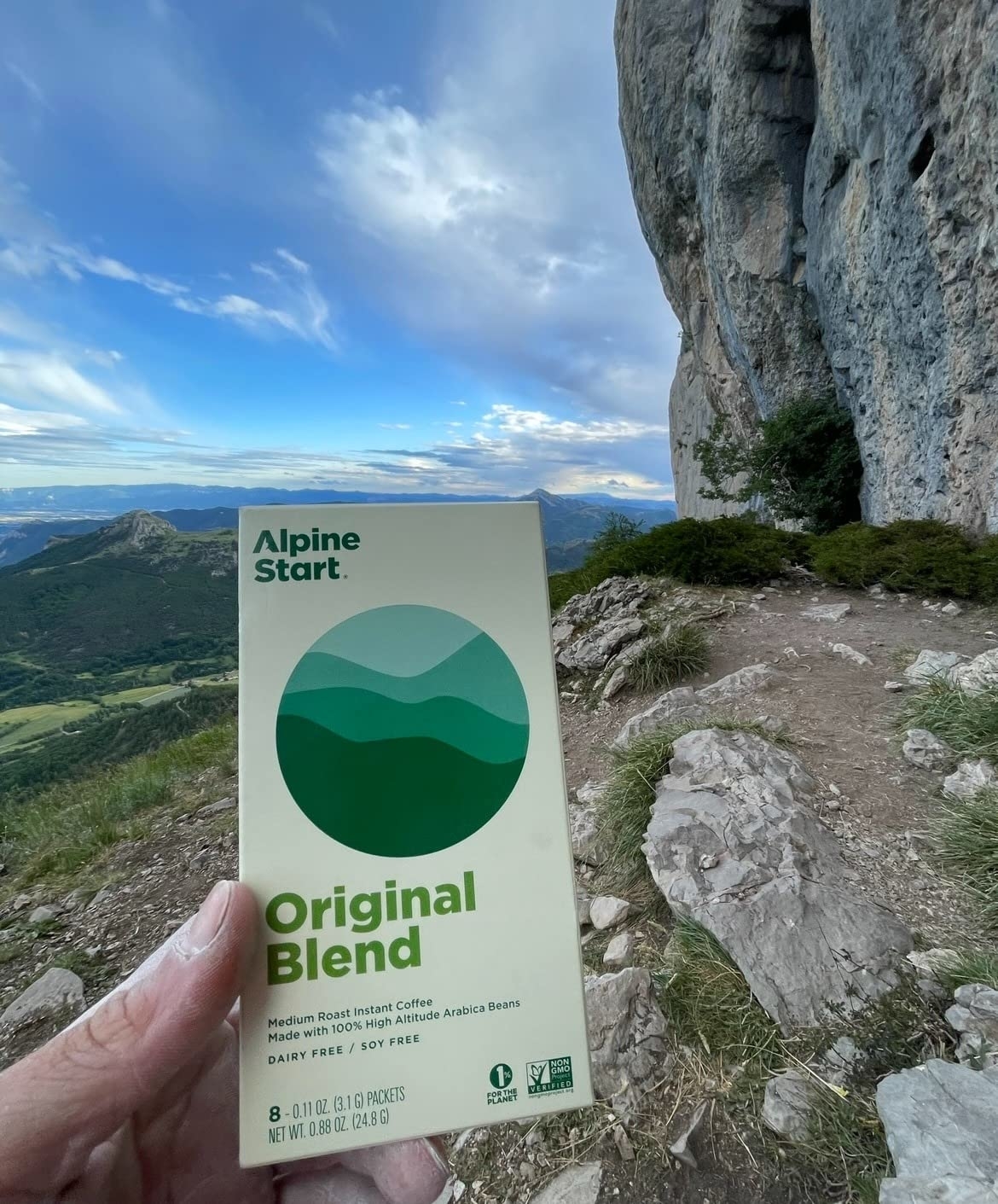 Hand holding a packet of Alpine Start Original Blend instant coffee on a mountain trail