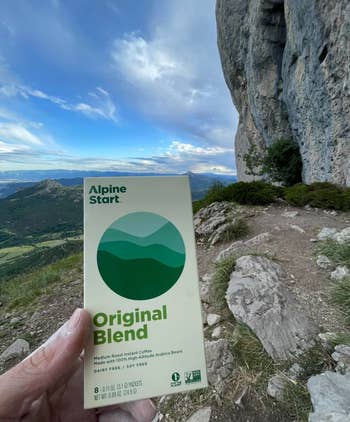 Hand holding a packet of Alpine Start Original Blend instant java  connected  a upland  trail