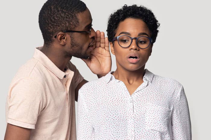 A person whispering into another person's ear, both showing surprised expressions