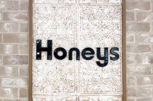 レンガ壁に取り付けられた装飾的な模様のあるドアに「Honeys」と書かれたサインが掲げられています。