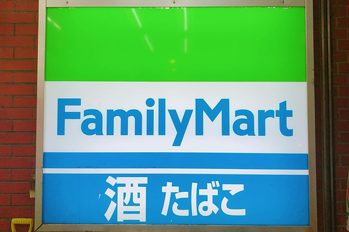 ファミリーマートの看板、緑と青のロゴに店名と日本語で「満たされて」の文字。