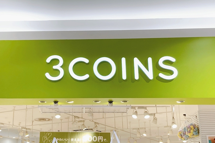 画像内のテキスト：3COINSストアの看板、300円均一の商品を提供する店舗の前面。